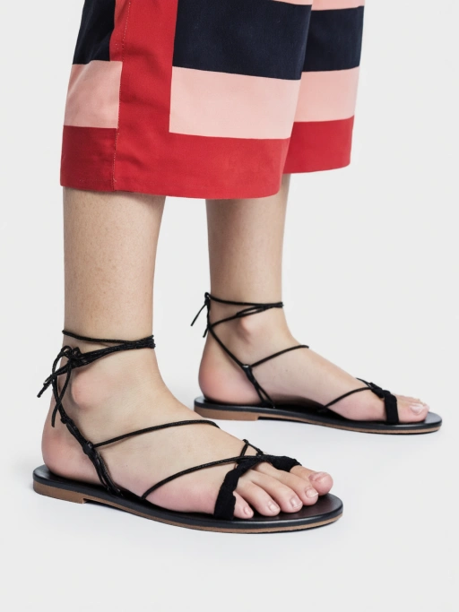 白無限背景上にベアフットで履かれたブラックストラピーグリップフラットサンダル、ラテラルサイドビュー。