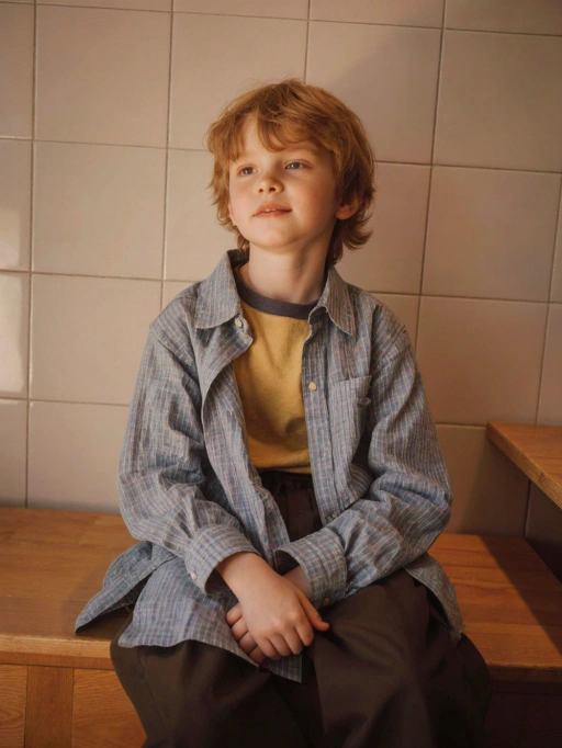 Este es un modelo infantil masculino reflexivo de Gran Bretaña, con cabello corto ondulado de color rubio rojizo, piel clara y figura delgada. Su atuendo consiste en un estilo casual en capas con una camisa de cuadros sobre una camiseta amarilla mostaza, combinado con pantalones oscuros. Su postura y mirada hacia arriba transmiten una sensación de curiosidad e introspección, lo que lo hace adecuado para campañas de moda orientadas a la familia, anuncios de ropa infantil o fotografía de estilo de vida que enfatiza la inocencia y el encanto natural.