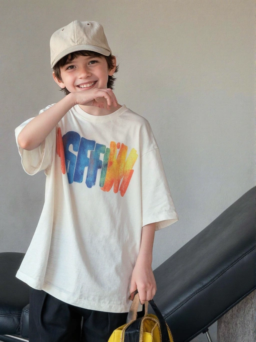 Este é um modelo infantil masculino brincalhão e alegre das Américas, provavelmente americano, com cabelo castanho curto e ondulado, pele clara e uma figura esguia. Seu sorriso alegre e pose casual transmitem uma sensação de alegria e vivacidade, tornando-o altamente adequado para moda infantil, fotografia de estilo de vida ou campanhas publicitárias voltadas para um público jovem e energético. As cores vibrantes de sua camiseta acrescentam à vibração geral alegre e dinâmica.
